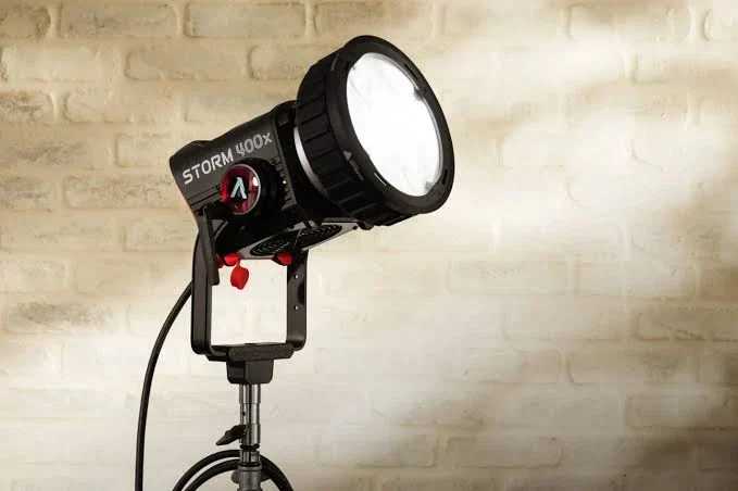 Моноблок Aputure STORM 400x на стійці з лінзою CF7 Fresnel та червоними захисними заглушками портів на фоні світлої цегляної стіни
